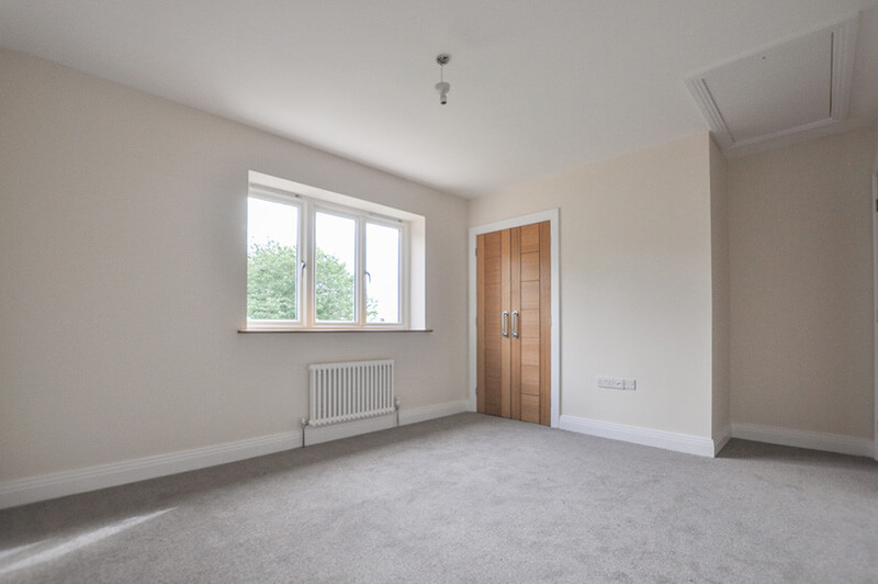 Spacious bedroom with white walls, in-built wardrobe and grey carpet.